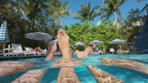 Relaxed feet floating in turquoise pool water with tropical resort background. Stock Footage 339802465