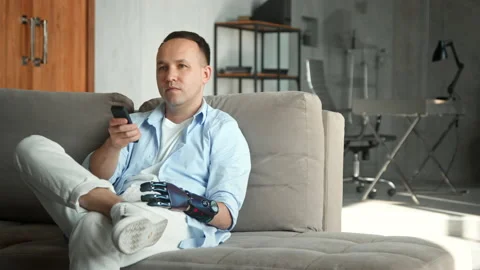 Relaxed man with bio hand prothesis takes remote controller Stock Footage 157533855