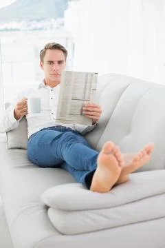 Relaxed man with coffee cup while reading newspaper on sofa Stock Photos
