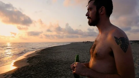 Relaxed Man Drinking Beer On The Beach,looking the sunset on the sea Stock Footage 76911427