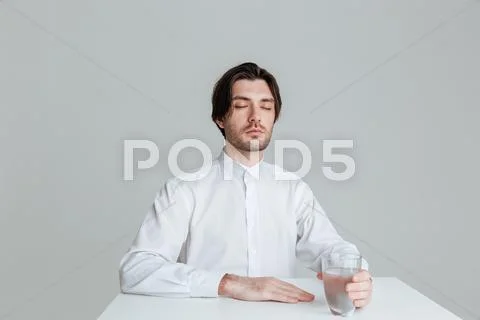 Relaxed man holding water glass while sitting at the table Stock Photos