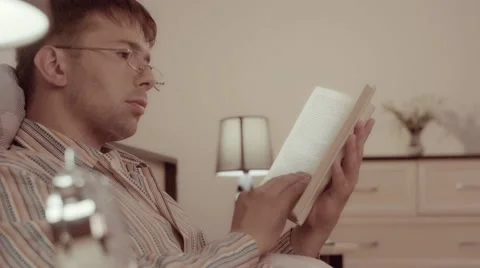 Relaxed man looking through the book in bed Stock-Footage 68420606