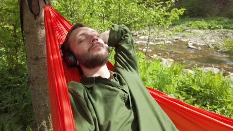 Relaxed man lying in hammock outdoor and listening music with wireless headphone Video stock 132012391
