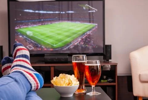 Relaxed man lying on sofa while watching football match on television at home Фото