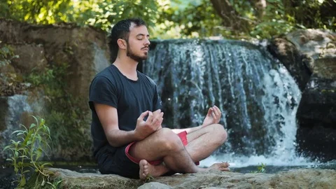 Relaxed man making lotus position near the waterfall Stock Footage 83959947