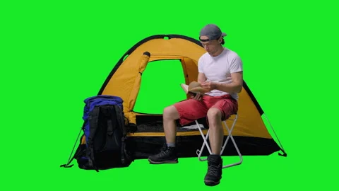Relaxed man reading book in front of tourist tent in campsite, chroma key Stock Footage 155395413