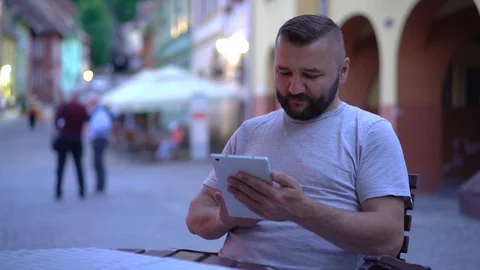 Relaxed man sitting in the cafe in old town and browsing internet on tablet Stock Footage 103519101