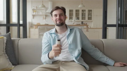 Relaxed Man Sitting On Sofa And Switching TV Channels With Remote Control Stock Footage 331792925