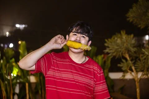 Relaxed Man Snacking on Grilled Corn. Man Enjoying Grilled Corn Under Night.. Stock Photos