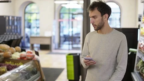 Relaxed man walking through the store looking at the screen of his smartphone Stock Footage 166894430
