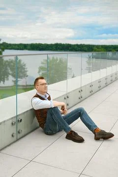 Relaxed middle-aged man sitting by lake on modern terrace during cloudy weath 库存照片