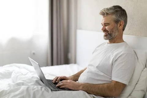 Relaxed middle aged man using laptop in bed Foto stock