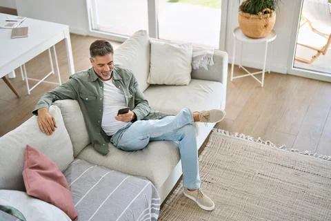 Relaxed middle aged man using mobile phone sitting at home on couch. Top view Stock Photos