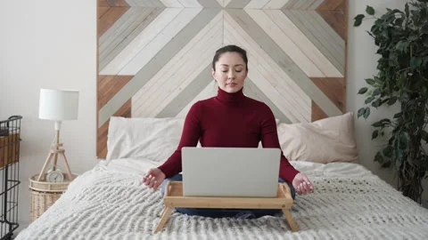 Relaxed mixed race young asian woman sitting on her bed with folded in mudra Stock Footage 169694094