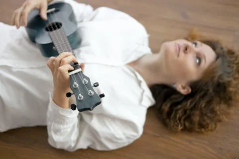 A relaxed person playing a ukulele while lying on a wooden floor in a cozy Foto stock