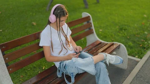 Relaxed preteen using digital tablet sitting on park bench outdoors. 動画素材 340924798