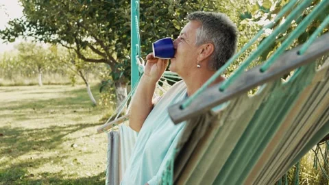 Relaxed woman drinking a refreshing beverage in a net hammock Video stock 343385645