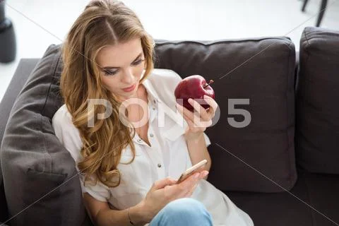 Relaxed Woman Eating Red Apple And Using Cell Phone