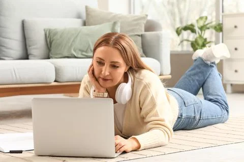 Relaxed woman lying on floor using laptop with headphones, remote work and on Stock Photos