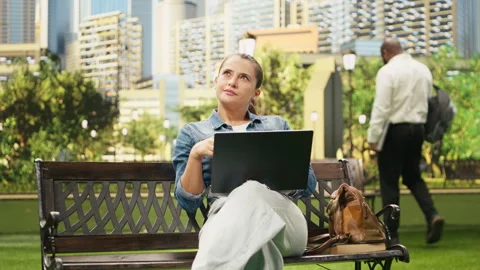 Relaxed woman using laptop for remote work while drinking coffee on bench Stock Footage 343499065