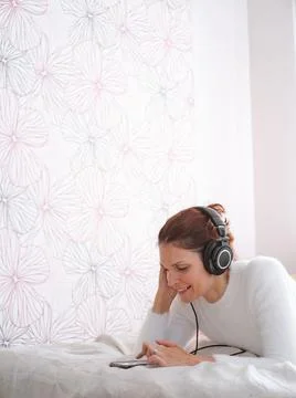 Relaxed woman using the mobile while listening to music in the bed Stock Photos