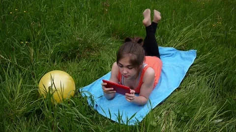 Relaxed young girl using digital tablet in country field. Cute teen lying on the Stock Footage
