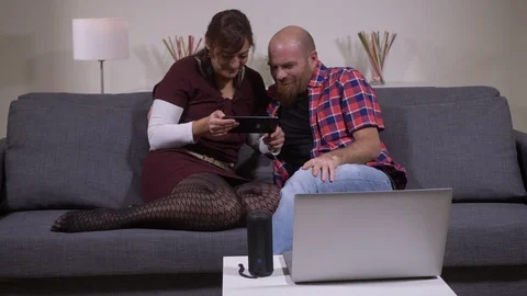 Relaxed young lovers sitting on sofa looking tablet and laughing 動画素材 107026879