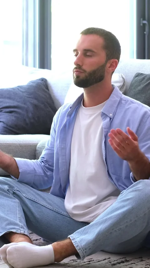 Relaxed young man with a beard sitting cross-legged on the floor of a modern Vídeos de archivo 344781256