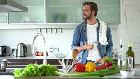 Relaxed young man drinking wine near table with fresh ingredients in kitchen Stock Footage 159535926