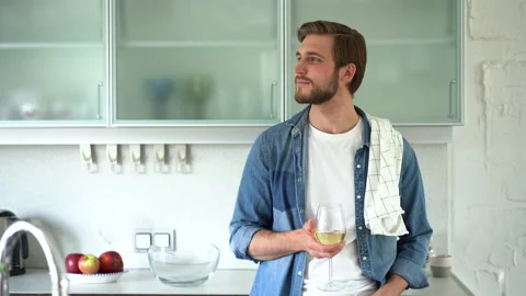 Relaxed young man drinking wine near table with fresh ingredients in kitchen Stock Footage 159536567