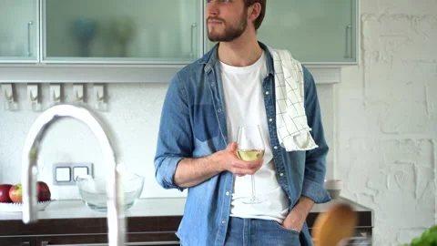 Relaxed young man drinking wine near table with fresh ingredients in kitchen Stock Footage 159537512