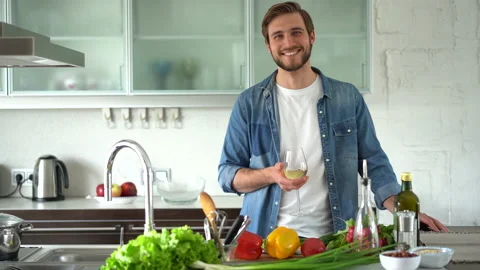 Relaxed young man drinking wine near table with fresh ingredients in kitchen Stock Footage 159551706