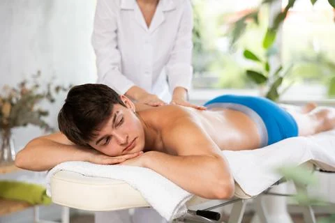 Relaxed young man having back massage therapy conducted by masseuse Stock Photos
