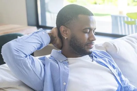 Relaxed young man resting on a couch at home, eyes closed and hand behind h.. Stock Photos
