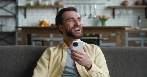 Relaxed young man sitting on sofa in living room, surfing internet on smartphone Stock Footage 196940883