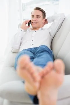 Relaxed young man using cellphone while lying on sofa Stock Photos