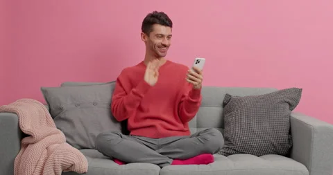 Relaxed young man waves palm in hello gesture makes video call via cellular and Stock Footage 143626285