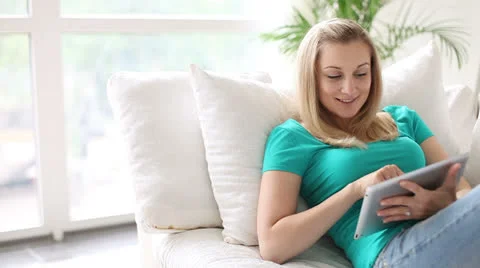 Relaxed young woman on sofa using touchpad and smiling at camera Stock Footage 25911587