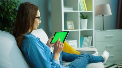 Relaxed young woman using black tablet computer with green screen while sitting Stock Footage 76359358