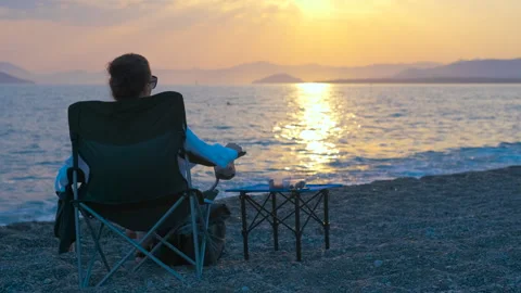 Relaxing on a beach watching the sunset over the sea Stock Footage 303449708