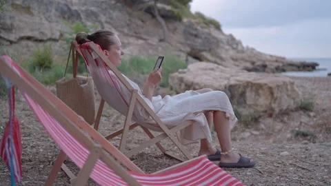 Relaxing by the beach while using a phone during the evening Stock Footage 346016600