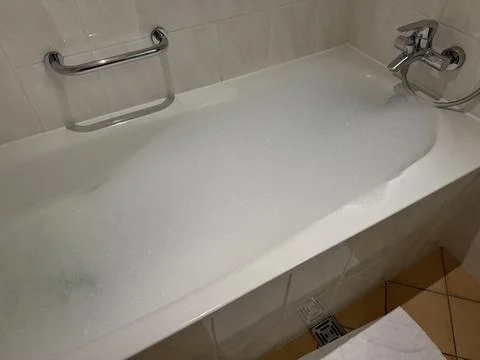 Relaxing bubble bath with foam and running water in clean white bathroom in.. Stock Photos