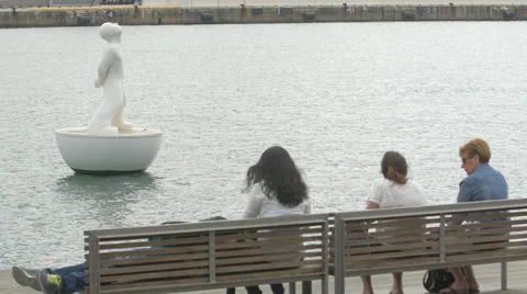 Relaxing in front of a statue floating on water in the old harbour of Barcelona Stock Footage 51460115