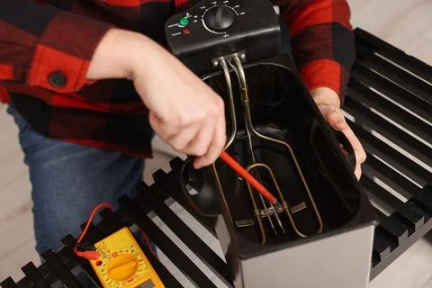 Relaxing hobby. Man testing deep fryer with multimeter indoors, closeup Stock Photos
