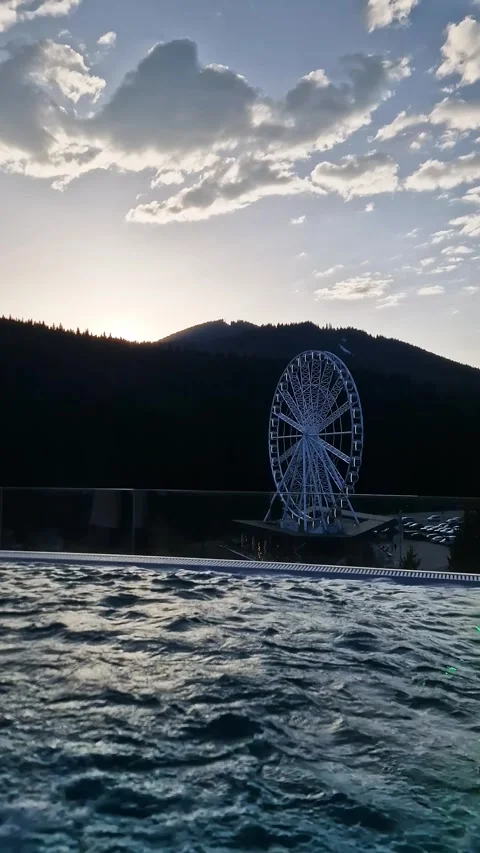 Relaxing Infinity Pool Overlooking Ferris Wheel and Mountains at Sunset Stock Footage 338994705
