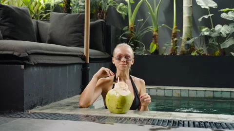 Relaxing in infinity pool resort drinking coconut juice. Rich woman luxury villa Stock Footage 238524931