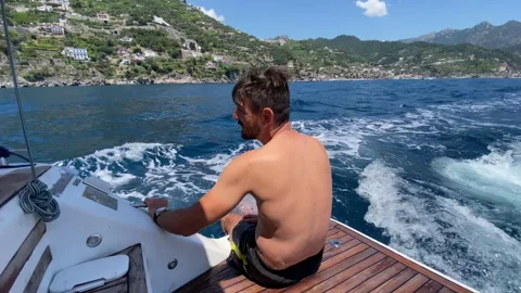 Relaxing man sitting on aft deck of sailing motorboat with legs put inside the Stock-Footage 316906733