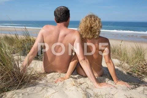Relaxing nudist couple sitting on beach under deep blue sky Stock Photos