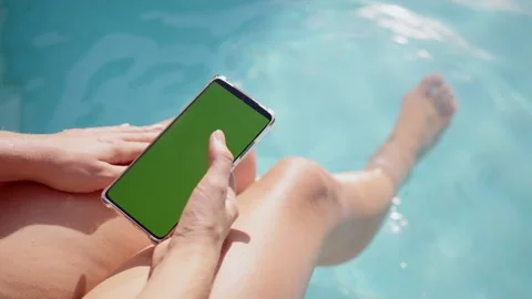 Relaxing summer day by the pool with smartphone with chromakey screen in hand Stock Footage 296715286