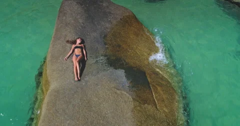 Relaxing by the turquoise waters while soaking up the sun on a large rock Stock Footage 315125424